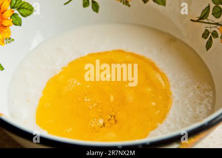 Öl, das in eine Metallschüssel in die Milch gegossen wird. Teigzubereitung. Rezeptpuffer-Gebäck. Backzutaten, Nahaufnahme, Draufsicht. Stockfoto