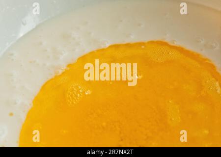 Öl, das in eine Metallschüssel in die Milch gegossen wird. Teigzubereitung. Rezeptpuffer-Gebäck. Backzutaten, Nahaufnahme, Draufsicht. Stockfoto