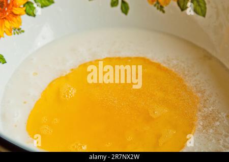 Öl, das in eine Metallschüssel in die Milch gegossen wird. Teigzubereitung. Rezeptpuffer-Gebäck. Backzutaten, Nahaufnahme, Draufsicht. Stockfoto