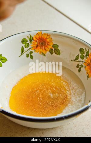 Öl, das in eine Metallschüssel in die Milch gegossen wird. Teigzubereitung. Rezeptpuffer-Gebäck. Backzutaten, Nahaufnahme, Draufsicht. Stockfoto
