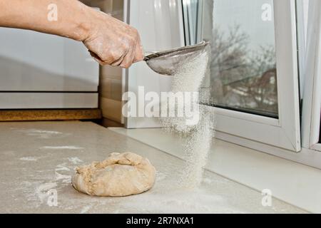 Weibliches Mehl, das von Hand durch ein manuelles Mehlsieb in einer Schüssel gesiebt wird, Nahkopie. Ich koche Teig. Küchengerät aus Metall. Stockfoto