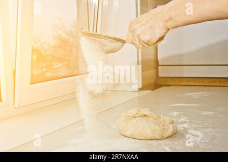 Weibliches Mehl, das von Hand durch ein manuelles Mehlsieb in einer Schüssel gesiebt wird, Nahkopie. Ich koche Teig. Küchengerät aus Metall. Stockfoto