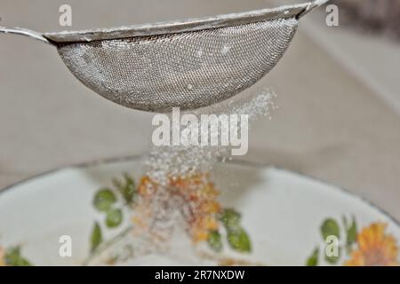 Weibliches Mehl, das von Hand durch ein manuelles Mehlsieb in einer Schüssel gesiebt wird, Nahkopie. Ich koche Teig. Küchengerät aus Metall. Stockfoto