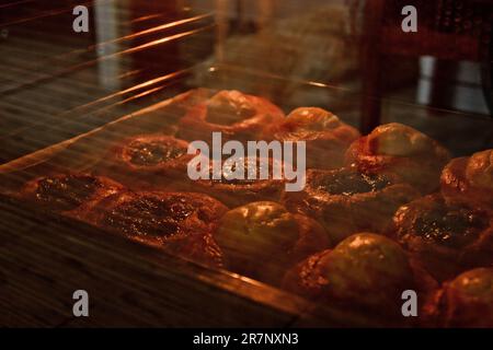 Ein Tablett voller Käsekuchen mit Hüttenkäse liegt im Ofen hinter dem Glas. Kochen Backen. Backphase. Nahaufnahme mit Reflexion Stockfoto