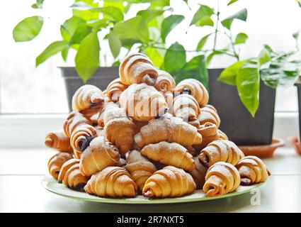 Brötchen auf einem Teller voller frisch gebackener Bagels mit Puderzucker auf dem Küchentisch. Kochen Backen. Croissants-Backphase Stockfoto