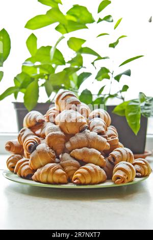 Brötchen auf einem Teller voller frisch gebackener Bagels mit Puderzucker auf dem Küchentisch. Kochen Backen. Croissants-Backphase Stockfoto