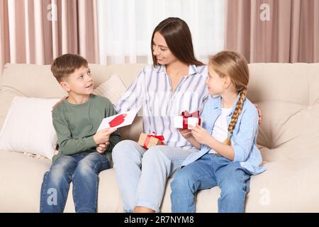 Süße kleine Kinder präsentieren ihrer Mutter zu Hause Geschenke auf dem Sofa Stockfoto