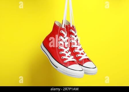 Ein Paar neue stylische rote Sneaker, die auf gelbem Hintergrund an Schnürsenkeln hängen Stockfoto