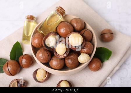 Schüssel mit Bio-Macadamia-Nüssen und natürlichem Öl auf weißem, strukturiertem Tisch, Ansicht oben Stockfoto
