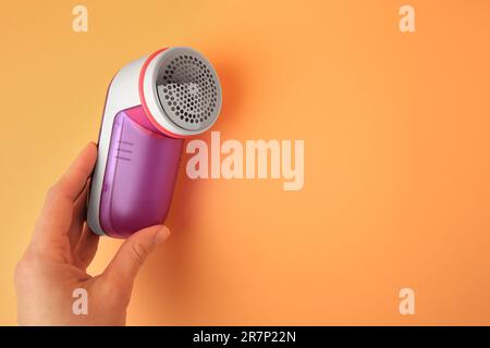 Eine Frau hält einen modernen Rasierer mit Stoff auf blassorangefarbenem Hintergrund, Nahaufnahme. Platz für Text Stockfoto