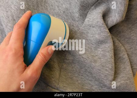 Frau, die einen modernen Stoffrasierer auf hellgrauem Tuch mit Fusseln und Nahaufnahme verwendet. Platz für Text Stockfoto