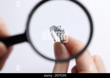 Juwelier untersucht Diamantring mit Lupe auf weißem Hintergrund, Nahaufnahme Stockfoto