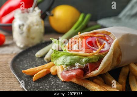 Köstliche Pita Wrap mit Prosciutto, Gemüse und Kartoffelfritten auf Holztisch, Nahaufnahme Stockfoto