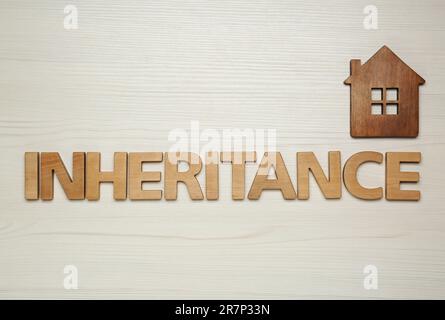 Wortvererbung mit Buchstaben und Hausmodell auf Holzhintergrund, flach liegend Stockfoto