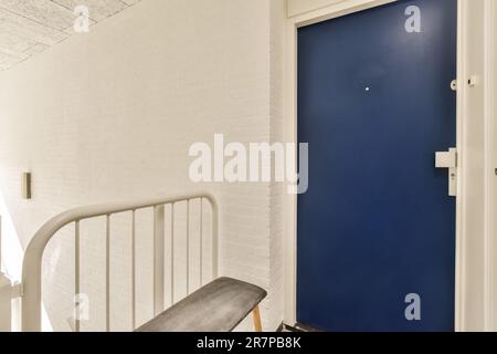 Eine blaue Tür und eine weiße Backsteinwand in einem Raum mit einer eisernen Bank neben der Vordertür, die gestrichen wurde Stockfoto
