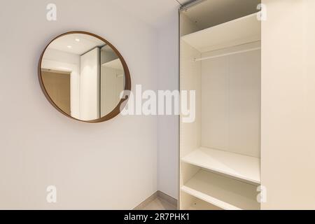 Nahaufnahme einer Zimmerecke mit Spiegel und einem offenen, leeren Kleiderschrank in hellen Beigetönen. Das Konzept einer komfortablen kompakten Wohnung danach Stockfoto