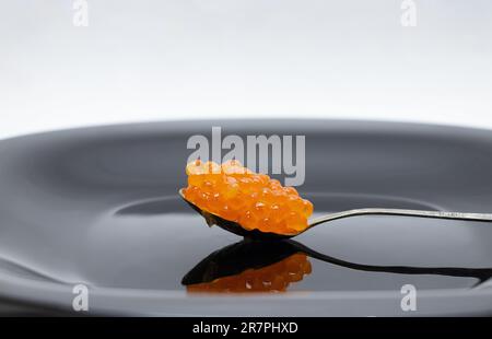 Löffel mit rotem Lachskaviar auf schwarzem Teller, Nahaufnahme Stockfoto