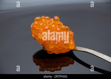 Löffel mit rotem Lachskaviar auf schwarzem Teller, Nahaufnahme Stockfoto