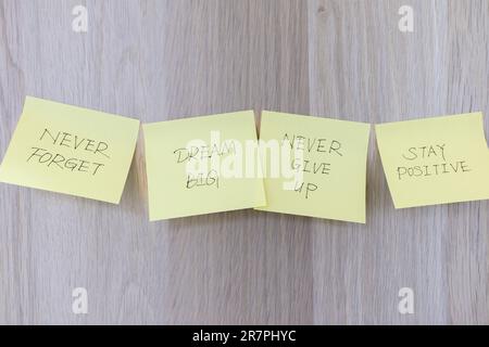 Inspirationskonzept, vier gelbe Haftnotizen auf dem Holzschreibtisch mit Motivationsbotschaften als Erinnerung an große Träume, niemals aufgeben und in Position bleiben Stockfoto