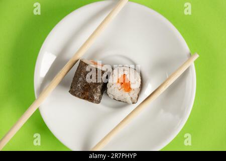 Sushi mit Lachs auf einem weißen Teller auf grünem Hintergrund, Nahaufnahme, Restaurantessen Stockfoto