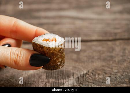 Sushi mit Lachs wird von einer weiblichen Hand auf weißem Hintergrund gehalten, Nahaufnahme, Restaurant-Essen Stockfoto