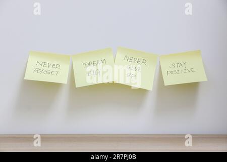 Vier gelbe Haftnotizen mit motivierenden und inspirierenden Botschaften, die über der weißen Wand über dem leeren Holzschreibtisch angebracht sind, Motivationskonzept Stockfoto
