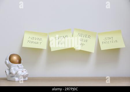 Vier gelbe Haftnotizen an der weißen Wand mit motivierenden und inspirierenden Botschaften neben einer Astronautenfigur, die „Never Forget t“ zum Ausdruck bringt Stockfoto