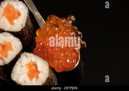 Sushi mit Lachs und rotem Kaviar in einem Löffel auf einem schwarzen Teller Stockfoto