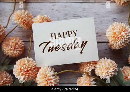 „Happy Tuesday“-Textnachricht mit Blumendekoration auf Holzhintergrund Stockfoto