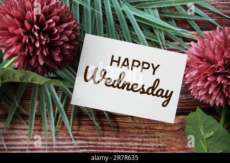 „Happy Wednesday“-SMS mit Blumendekoration auf Holzhintergrund Stockfoto