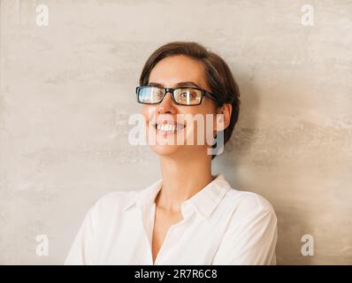 Porträt einer glücklichen kaukasischen Geschäftsfrau mit Brille, die sich an die Wand lehnt Stockfoto