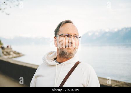 Portrait eines gutaussehenden Mannes, der einen wunderschönen See mit Bergen bewundert, mit weißem Sweatshirt Stockfoto