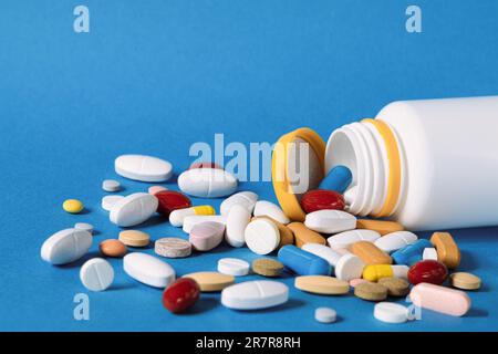 Viele Pillen sind aus einer Plastikflasche verschüttet worden. Mehrfarbige Pillen, die aus einer Plastikflasche auf blauem Hintergrund austreten. Eine Vielzahl von Pillen und Medikamenten. Stockfoto