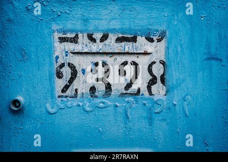 Leuchtend blauer Hausposten: Zahlen schmücken diesen auffälligen Hausposten und schaffen einen faszinierenden Blickpunkt vor dem leuchtend blauen Hintergrund. Stockfoto