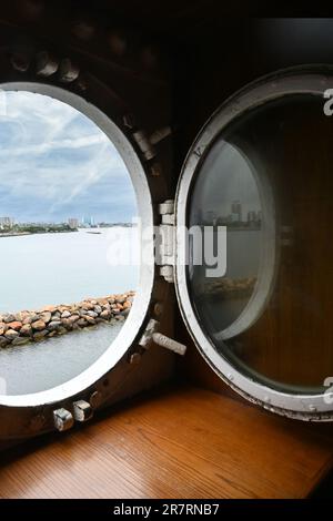 LONG BEACH, KALIFORNIEN - 14. JUNI 2023: Blick auf Port Hole auf der Queen Mary mit der Bucht und der Skyline von Long Beach in der Ferne. Stockfoto