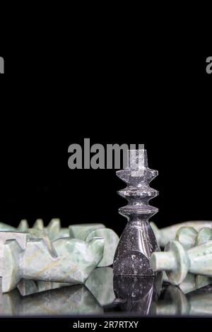 König besiegt alle anderen im Schachspiel, Symbol des Sieges mit Marmorschachfiguren auf schwarzem Hintergrund - mit Textraum Stockfoto