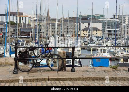 Auf dem gepflasterten West Pier auf Plymouth's Barbican befindet sich ein schwarzes Fahrrad, das auf den Geländern ruht. Weicher Fokus jenseits des Innenbeckens mit Yachten A Stockfoto