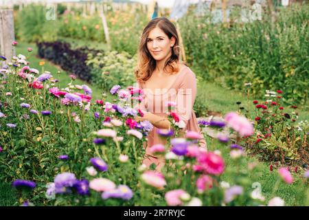 Hübsche junge Frau, die im Herbstgarten arbeitet, Mädchen, die sich um das bunte Chrysanthemum kümmert, Gärtner, die den warmen und sonnigen Tag genießen Stockfoto