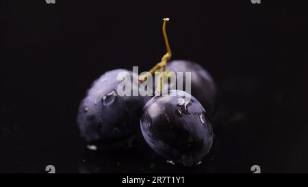 Nahaufnahme von drei Beeren dunkler Trauben mit Wassertropfen Stockfoto