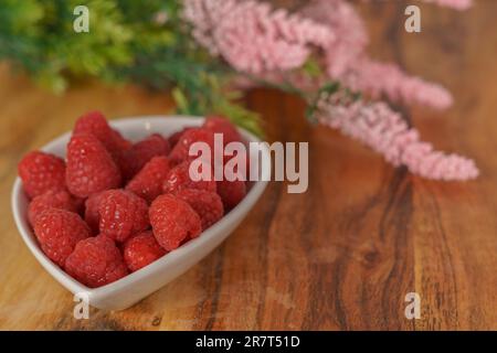 Himbeeren in einer weißen Keramikschüssel auf einem Holztisch Stockfoto