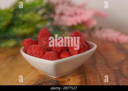 Himbeeren in einer weißen Keramikschüssel auf einem Holztisch Stockfoto