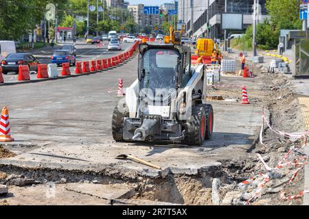 An einem sonnigen Tag parkt ein Baufahrzeug mit Presslufthammer in einem Bau- und Reparaturbereich vor dem Hintergrund einer Stadtstraße. Stockfoto