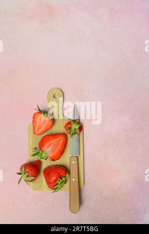 Whole and halved strawberries (Fragaria) with kitchen knife on wooden board Stockfoto