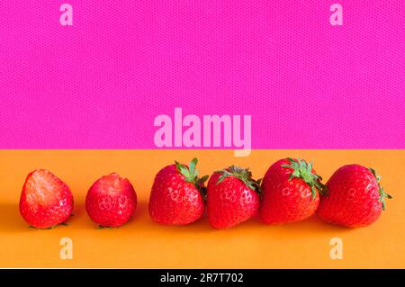 Eine Reihe frischer Erdbeeren auf einem lebhaften farbigen Hintergrund, kostenloser Kopierraum, Obst, gesunde Lebensmittel, Sommerkonzept. Stockfoto