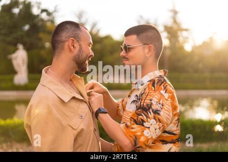 Ein homosexuelles Paar, das sich gegenseitig küsst und den Sonnenuntergang in einem Park in der Stadt ansieht. Diversität und lgbt-Konzept Stockfoto
