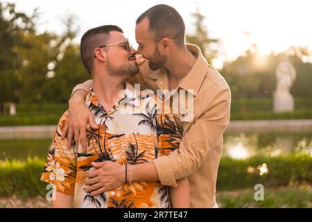 Ein homosexuelles Paar, das sich gegenseitig küsst und den Sonnenuntergang in einem Park in der Stadt ansieht. Diversität und lgbt-Konzept Stockfoto