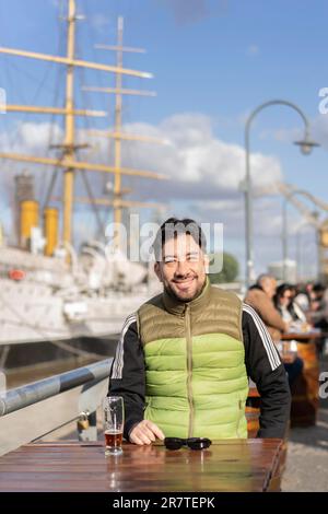 Porträt eines lächelnden Mannes, der in einer Bar am Hafen sitzt Stockfoto