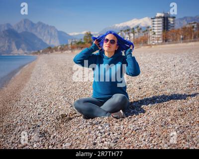 Eine Frau trägt einen hellblauen Hoodie und Jeans in Übergröße. Blauhaarige Frau draußen im Park am Strand von Antalya. Kleidungsmodell, leerer Platz für Text o Design. Stockfoto