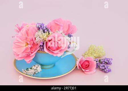 Surreales Design mit Rosen-, Baldrian-, Lavendel- und älteren Blüten in einer Teetasse auf Pink. Spaßige pflanzliche Medizin-Zusammensetzung. Stockfoto