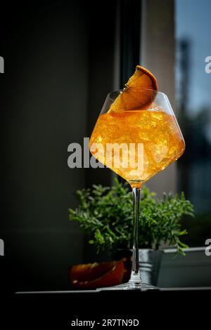 Ein Glas Aperol Spritz Cocktail mit frischen Orangen am Fenster. Natürliches Licht und Schatten Stockfoto